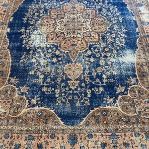 May include: A distressed, rectangular rug with a central medallion design. The rug features a deep blue field with faded areas, and a border in shades of brown and peach. Floral and geometric patterns are visible throughout.