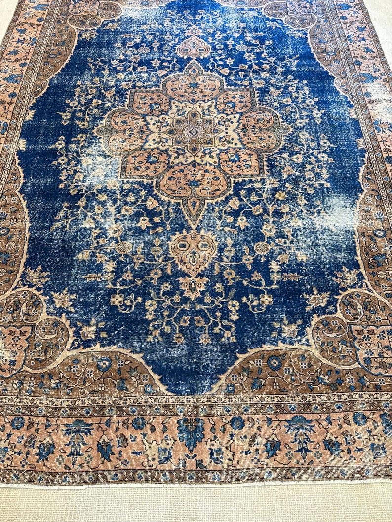 May include: A distressed, rectangular rug with a central medallion design. The rug features a deep blue field with faded areas, and a border in shades of brown and peach. Floral and geometric patterns are visible throughout.
