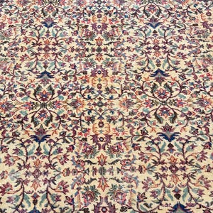 May include: An ornate, beige rug with a detailed floral pattern in shades of purple, blue, and green. The rug's design features a repeating motif of stylized flowers and leaves, creating a classic, elegant look. The rug is suitable for living rooms and bedrooms.