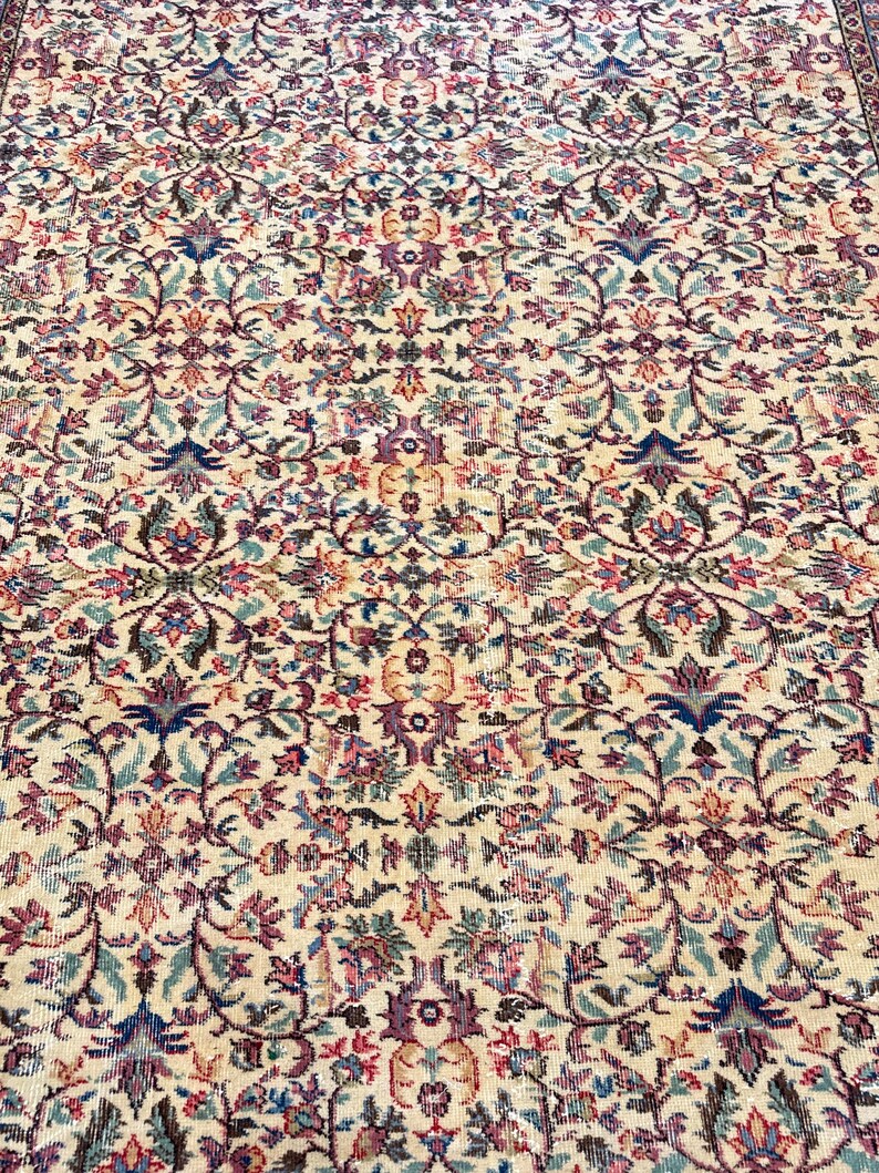 May include: An ornate, beige rug with a detailed floral pattern in shades of purple, blue, and green. The rug's design features a repeating motif of stylized flowers and leaves, creating a classic, elegant look. The rug is suitable for living rooms and bedrooms.