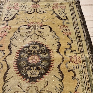 May include: A vintage area rug with a beige background and intricate floral patterns in shades of brown, red, and green. The rug features a central medallion design and a detailed border, showcasing a classic, aged aesthetic.