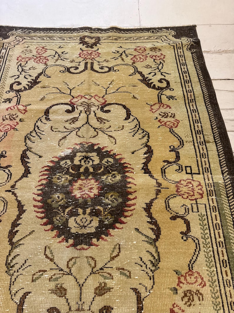May include: A vintage area rug with a beige background and intricate floral patterns in shades of brown, red, and green. The rug features a central medallion design and a detailed border, showcasing a classic, aged aesthetic.