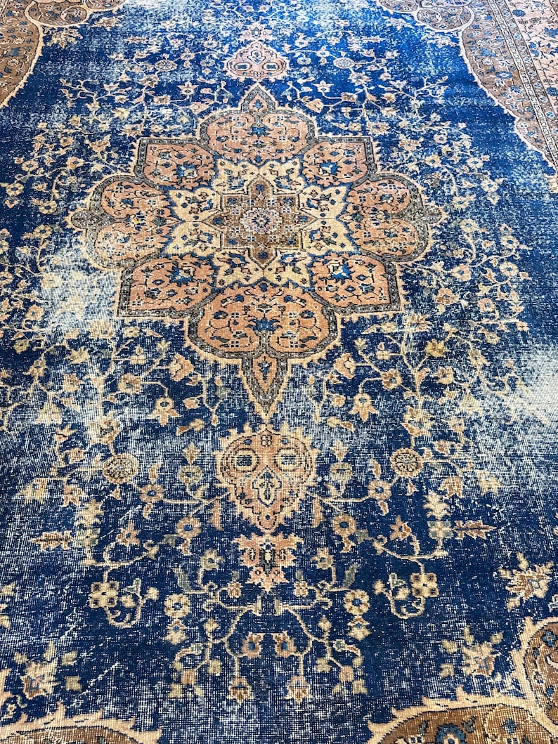 May include: A distressed, vintage-style rug with a central medallion design. The rug features a deep blue field with intricate floral patterns in beige and peach tones. The rug's design includes a border with similar colors and patterns.