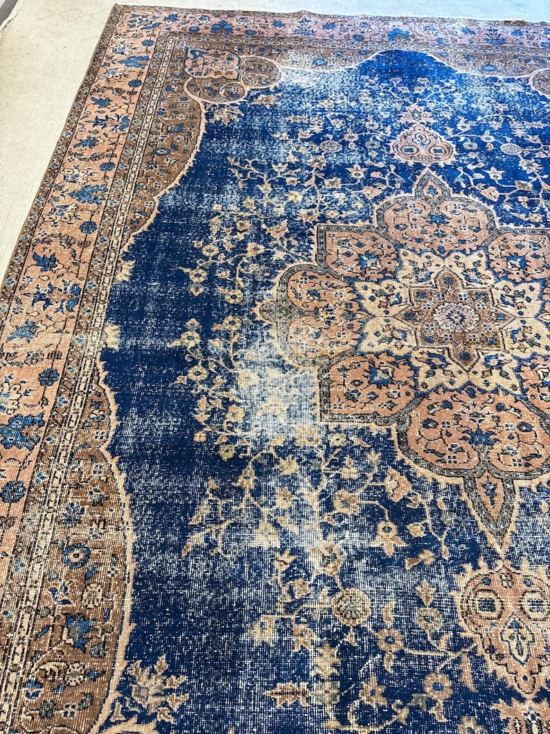 May include: A distressed, vintage-style rug with a central navy blue field and intricate floral patterns in shades of peach, brown, and cream. The rug features a detailed border and a faded, antique appearance, suitable for home decor.