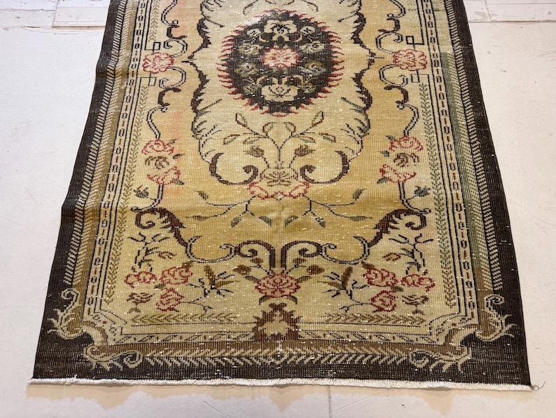 May include: A rectangular, vintage-style rug with a central medallion design. The rug features a cream-colored field with floral and scroll motifs in shades of brown, red, and green. The border is a dark brown with a repeating pattern.