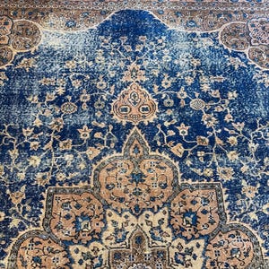May include: A distressed, vintage rug with a rich navy blue central field. The rug features intricate floral and geometric patterns in shades of peach, brown, and cream. The border has a faded, aged appearance, adding to its antique charm.