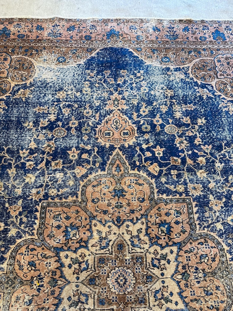 May include: A distressed, vintage rug with a rich navy blue central field. The rug features intricate floral and geometric patterns in shades of peach, brown, and cream. The border has a faded, aged appearance, adding to its antique charm.