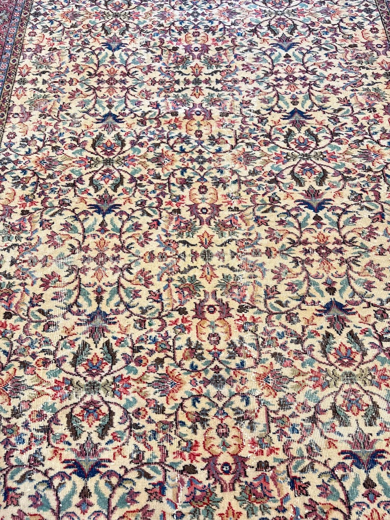 May include: An antique rug with an intricate floral pattern. The rug features a cream-colored background with a repeating design of flowers and leaves in shades of blue, pink, and green. The rug has a detailed border.
