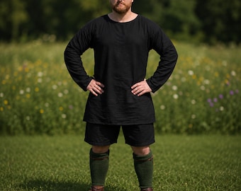 May include: A black tunic and shorts ensemble. The long-sleeved tunic has a crew neck and falls to mid-thigh. The shorts are knee-length. The outfit is paired with green knee-high socks and brown boots. The person is standing in a grassy field.