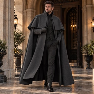 May include: A charcoal gray wool-blend floor-length cape coat featuring a structured collar, a button-front closure, and a layered shoulder design. The garment is worn over a matching charcoal gray vest, dark trousers, and black leather boots.