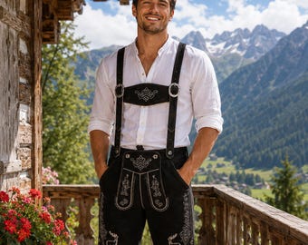 Puede incluir: Una camisa blanca de manga larga con botones combinada con pantalones de cuero negro que presentan intrincados bordados blancos de ciervos y motivos florales, una pechera frontal y tirantes ajustables con hebillas metálicas plateadas.