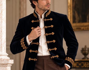 May include: A dark navy blue velvet jacket featuring a high collar and gold braided cord closures. The jacket is adorned with intricate gold leaf embroidery on the collar and cuffs, worn over a crisp white button-down shirt and brown trousers.
