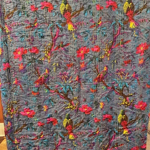 May include: A gray, floral patterned quilt featuring red flowers and colorful birds perched on branches. The quilt has a stitched design and is made of a soft material. The quilt is approximately 80 inches long and 60 inches wide.