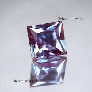 May include: A square-cut gemstone with a reflective surface. The gem displays a mix of purple and blue hues, with facets catching the light. The text "RehamaniJewels" is visible in the image.