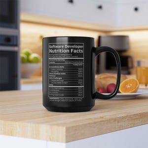 Peut inclure: Un mug en céramique noir avec un texte blanc imitant une étiquette de valeur nutritionnelle intitulée Software Developer Nutrition Facts, listant diverses compétences et défis quotidiens comme le débogage et la dépendance au café.