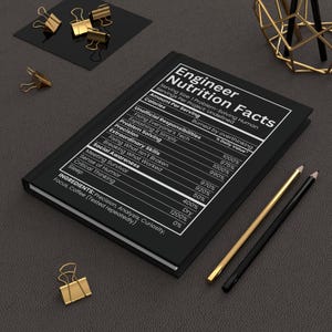 Op de afbeelding: Een zwart notitieboek met de titel "Engineer Nutrition Facts" in witte tekst, met vermelding van "Unofficial Responsibilities" en "Extraordinary Skills". Gouden en zwarte potloden en gouden paperclips liggen op een donkere ondergrond.