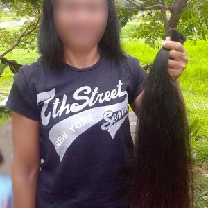 Puede incluir: Una persona sostiene un mech&oacute;n de cabello casta&ntilde;o oscuro. La persona lleva una camiseta negra con el texto "7th Street New York Sens". El cabello es largo y liso. El fondo es una escena borrosa al aire libre.