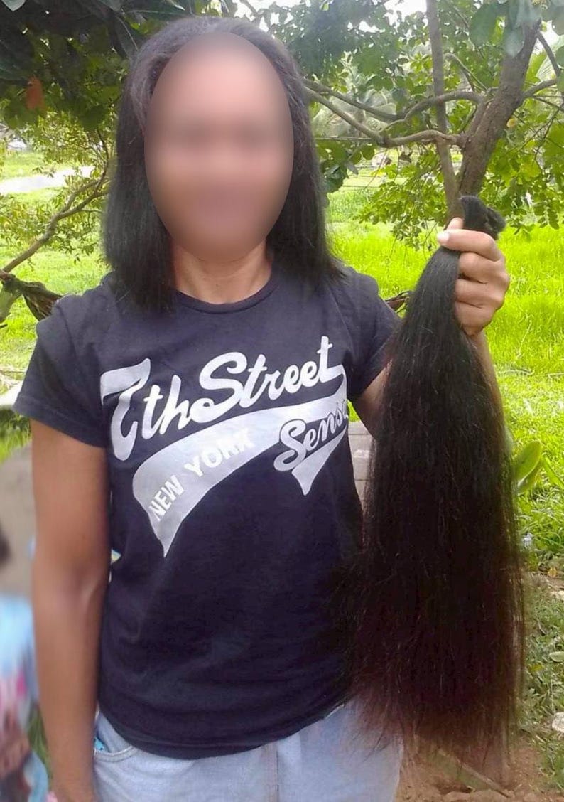 Puede incluir: Una persona sostiene un mech&oacute;n de cabello casta&ntilde;o oscuro. La persona lleva una camiseta negra con el texto "7th Street New York Sens". El cabello es largo y liso. El fondo es una escena borrosa al aire libre.