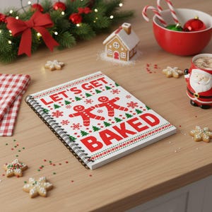 May include: A festive spiral-bound notebook with a Christmas theme. The cover displays the text "LET'S GET BAKED" with gingerbread men and holiday patterns in red and green. The notebook is on a wooden surface with Christmas decorations.