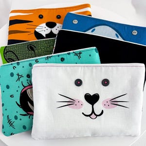May include: A collection of colorful fabric pouches, each featuring a whimsical animal face design. The pouches include a tiger, dinosaur, shark, and bunny, with button eyes and detailed facial features. The pouches are in various colors, including orange, blue, and teal.