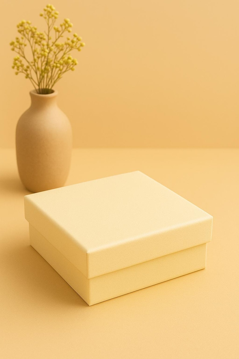 May include: A square, pale yellow gift box with a matching lid sits on a pale yellow surface. A small, tan vase holds a bouquet of yellow flowers, set against a pale yellow background.