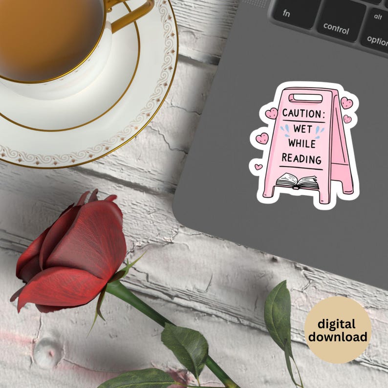 May include: A pink sticker with the text "CAUTION: WET WHILE READING" on a caution sign, with hearts and a book illustration. A red rose, a teacup, and a laptop are also in the image.