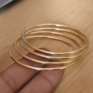 Conjunto minimalista de brazaletes dorados, pulseras finas apilables, joyería pulida para el día a día.