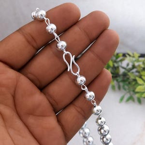 May include: A silver beaded necklace with a hook clasp. The necklace is composed of small, round, shiny beads strung together. The clasp is a simple, elegant design.