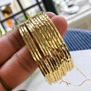 Conjunto de brazaletes dorados martillados, pulseras finas apilables, joyería minimalista texturizada.