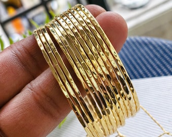 Conjunto de brazaletes dorados martillados, pulseras finas apilables, joyería minimalista texturizada.