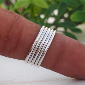 Pu&ograve; includere: Una pila di sei anelli color argento, ciascuno con una superficie liscia e lucida. Gli anelli sono indossati su un dito, con uno sfondo verde sfocato. Gli anelli sono semplici ed eleganti, adatti all'uso quotidiano.