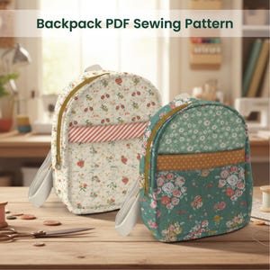 Op de afbeelding: Twee kleine, gewatteerde rugzakken met bloempatronen en gouden ritsen staan op een houten oppervlak. Eén rugzak heeft een crèmekleurige achtergrond met rode aardbeien, de andere is groen met rozen. De tekst "Backpack PDF Sewing Pattern" staat bovenaan.
