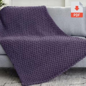 May include: A woven, purple blanket draped over a gray sofa. The blanket has a thick, textured weave pattern. The blanket is a solid color and appears soft and cozy. The PDF icon is in the upper right corner.