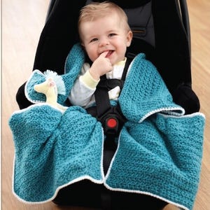May include: A baby in a car seat is wrapped in a teal crocheted blanket with a white border. A stuffed toy is tucked in the blanket. The baby is smiling and wearing a white onesie.