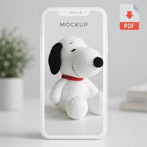 May include: A white and black crocheted Snoopy plush toy with a red collar is displayed on a phone screen. The phone is on a white surface. The word "MOCKUP" is at the top of the screen. A PDF icon is in the upper right corner.