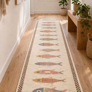 May include: A long, rectangular runner rug featuring an off-white base with a repeating pattern of stylized fish in shades of blue, pink, and yellow. The rug is framed by a dark brown geometric border and finished with fringe on both ends.