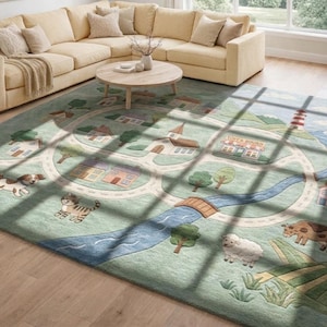 May include: A rectangular area rug with a town and road design. The rug features a light green background with a road, houses, a church, a lighthouse, and cartoon animals. The rug is placed on a hardwood floor.