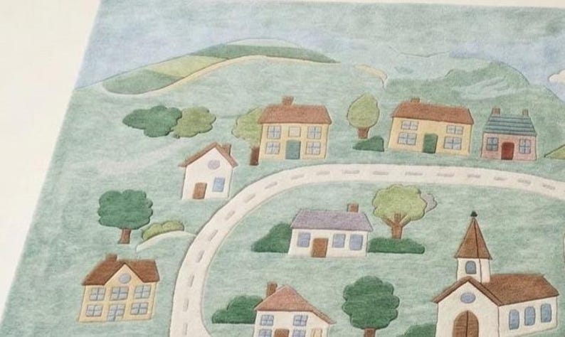 May include: A watercolor-style illustration of a small town with houses, trees, and a winding road. The houses have brown, yellow, and white exteriors with blue and yellow windows. A church with a steeple is also visible.