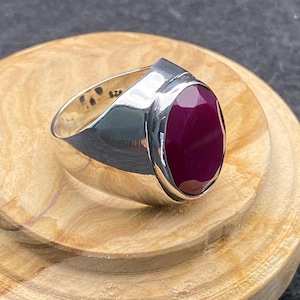 Peut inclure: Une bague en argent avec une grosse pierre précieuse rouge foncé de forme ovale. La bague a une finition polie et un design moderne. La pierre précieuse est le point central, sertie dans une lunette lisse.
