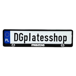 Peut inclure: Plaque d'immatriculation noire avec une plaque blanche portant le texte "DGplatesshop". La plaque comporte un symbole bleu de l'Union européenne et "PL" à gauche. Le logo Mazda est centré en bas.