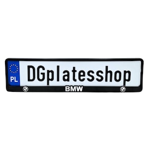 Pode incluir: Uma moldura retangular preta para placa de licença com o texto "DGplatesshop" em letras pretas em negrito. A moldura tem um fundo branco e apresenta o logotipo e o texto da BMW. A moldura também inclui um símbolo azul da União Europeia e as letras "PL".