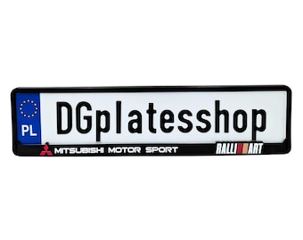 May include: A rectangular license plate with a black border. The plate is white with the text "DGplatesshop" in bold black letters. Below the text is "MITSUBISHI MOTOR SPORT" and "RALLI ART". The plate also has a blue EU symbol and "PL" on the left.
