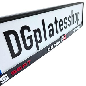 Puede incluir: Placa de matr&iacute;cula blanca con letras negras en relieve "DGplateshop". La placa tiene un borde negro y presenta las palabras "CUPRA R" y "SEAT" en letras rojas y blancas.