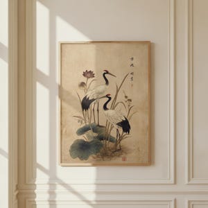 Puede incluir: Una impresi&oacute;n enmarcada con dos grullas japonesas entre hojas y flores de loto. La obra de arte tiene una est&eacute;tica vintage con tonos apagados de beige, negro y rojo. Las grullas son el punto focal, con representaciones detalladas de sus plumas y picos.
