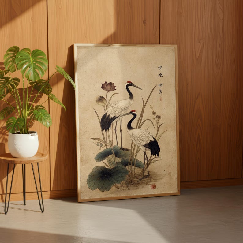 Puede incluir: Obra de arte enmarcada con dos grullas con coronas rojas y puntas de alas negras, de pie entre hojas de loto y juncos. La obra de arte tiene una est&eacute;tica vintage con un fondo beige y un marco de madera. El estilo recuerda al arte asi&aacute;tico tradicional.