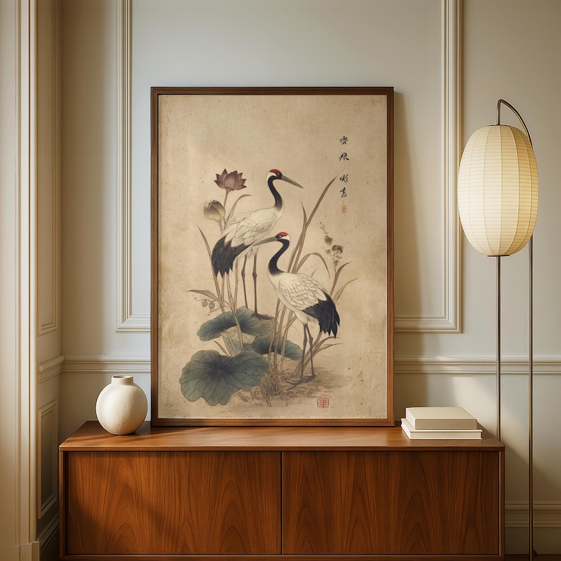 Puede incluir: Una obra de arte enmarcada con dos grullas entre flores de loto y follaje. Las grullas tienen plumaje blanco y negro con detalles rojos. La obra est&aacute; en un marco de madera y tiene una est&eacute;tica vintage.