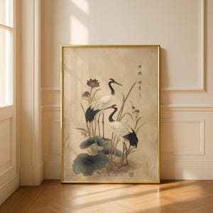 Puede incluir: Una impresi&oacute;n enmarcada que presenta dos elegantes grullas con coronas rojas, plumaje blanco y negro y largas patas, de pie entre hojas de loto y juncos. La obra de arte tiene una est&eacute;tica vintage con colores suaves y caligraf&iacute;a asi&aacute;tica tradicional.
