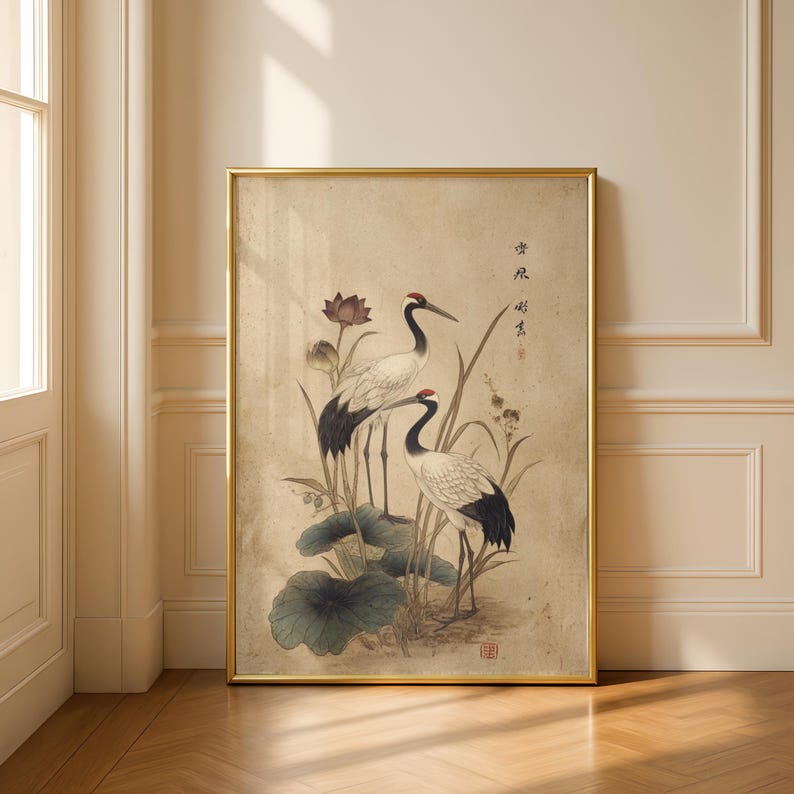 Puede incluir: Una impresi&oacute;n enmarcada que presenta dos elegantes grullas con coronas rojas, plumaje blanco y negro y largas patas, de pie entre hojas de loto y juncos. La obra de arte tiene una est&eacute;tica vintage con colores suaves y caligraf&iacute;a asi&aacute;tica tradicional.