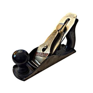 May include: A vintage Stanley Handyman smoothing plane. The metal blade and body show signs of wear, with the text "STANLEY HANDYMAN" visible. The handle and knob are black, and the plane is set against a white background.