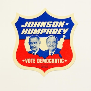May include: A vintage political campaign sticker featuring the text "JOHNSON-HUMPHREY" in white letters on a blue background. Below are portraits of two men, with the words "VOTE DEMOCRATIC" in white on a red background.